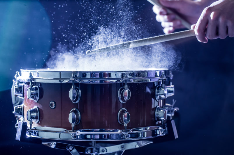 man plays musical percussion instrument with sticks closeup on a black background, a musical concept with the working drum, beautiful lighting on the stage